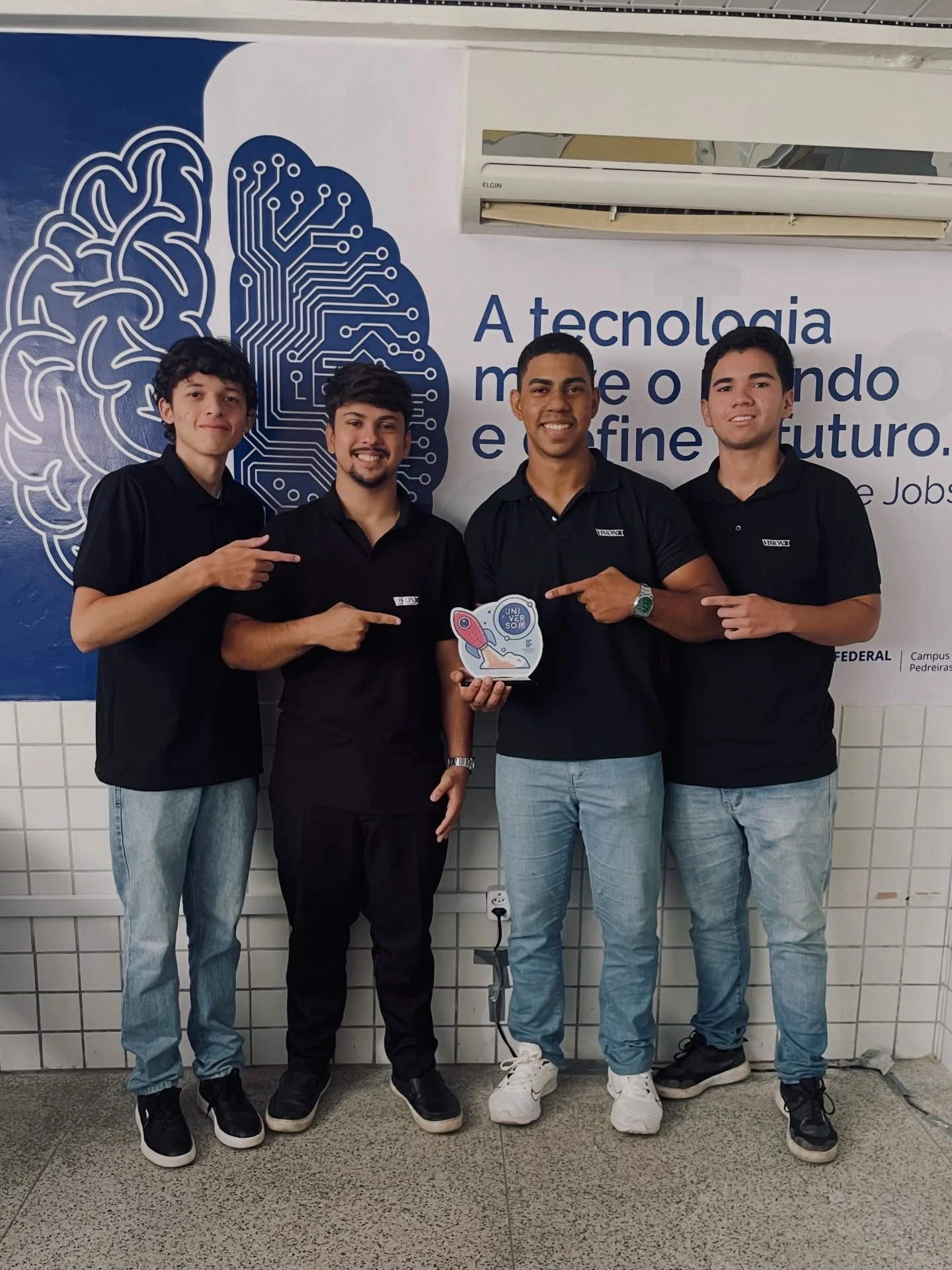 Equipe da VisionX posa com o troféu do Universo IF diante de um painel institucional sobre tecnologia, em Pedreiras (MA)