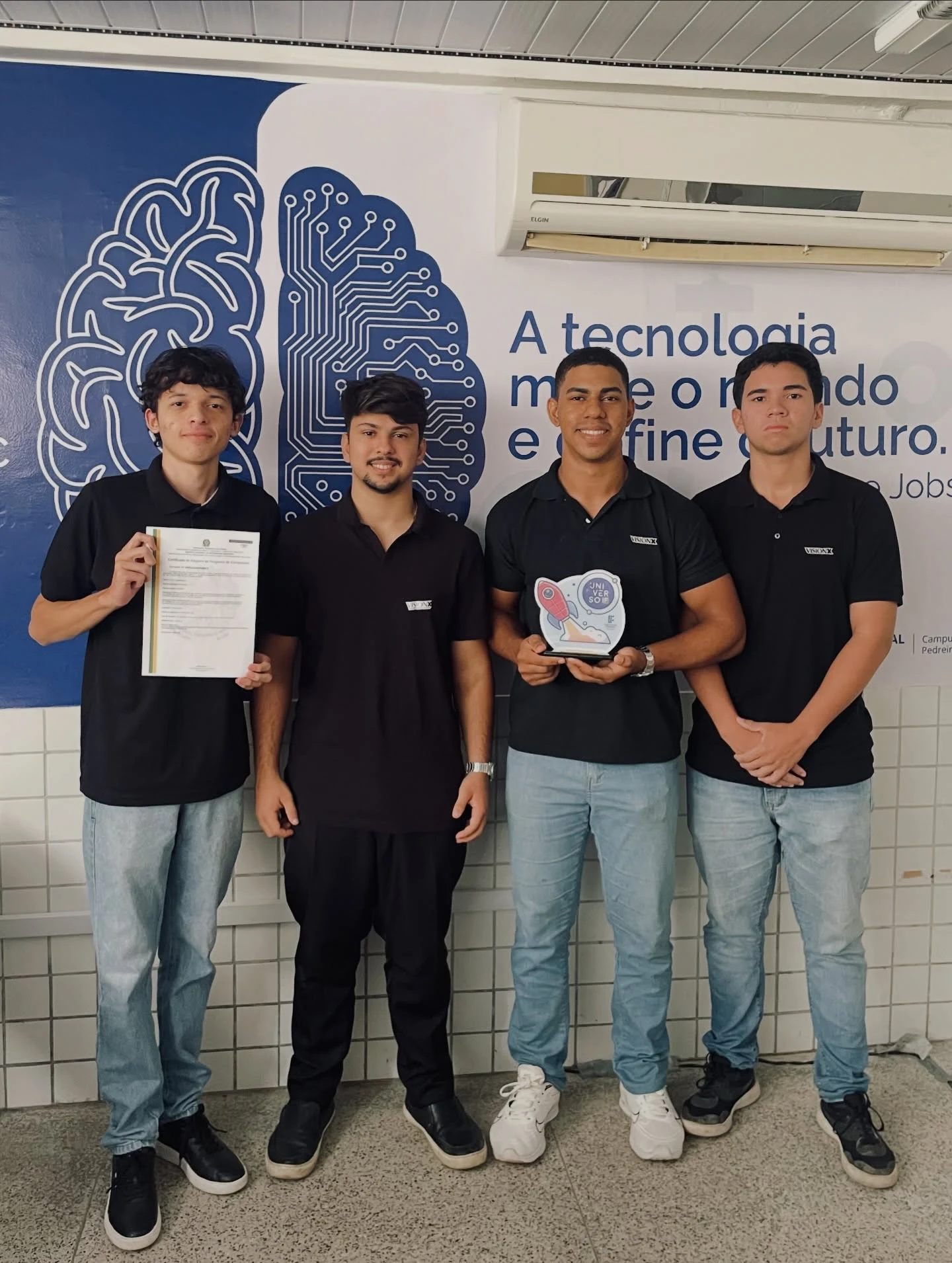 Integrantes da equipe exibem o troféu e o certificado do reconhecimento, no mesmo local