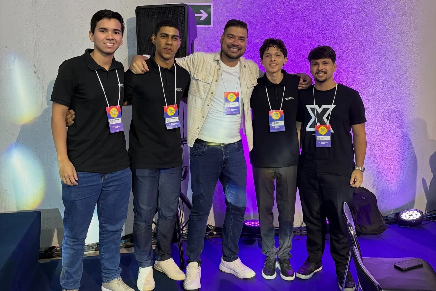 Cinco pessoas da equipe posam juntas em área iluminada do evento