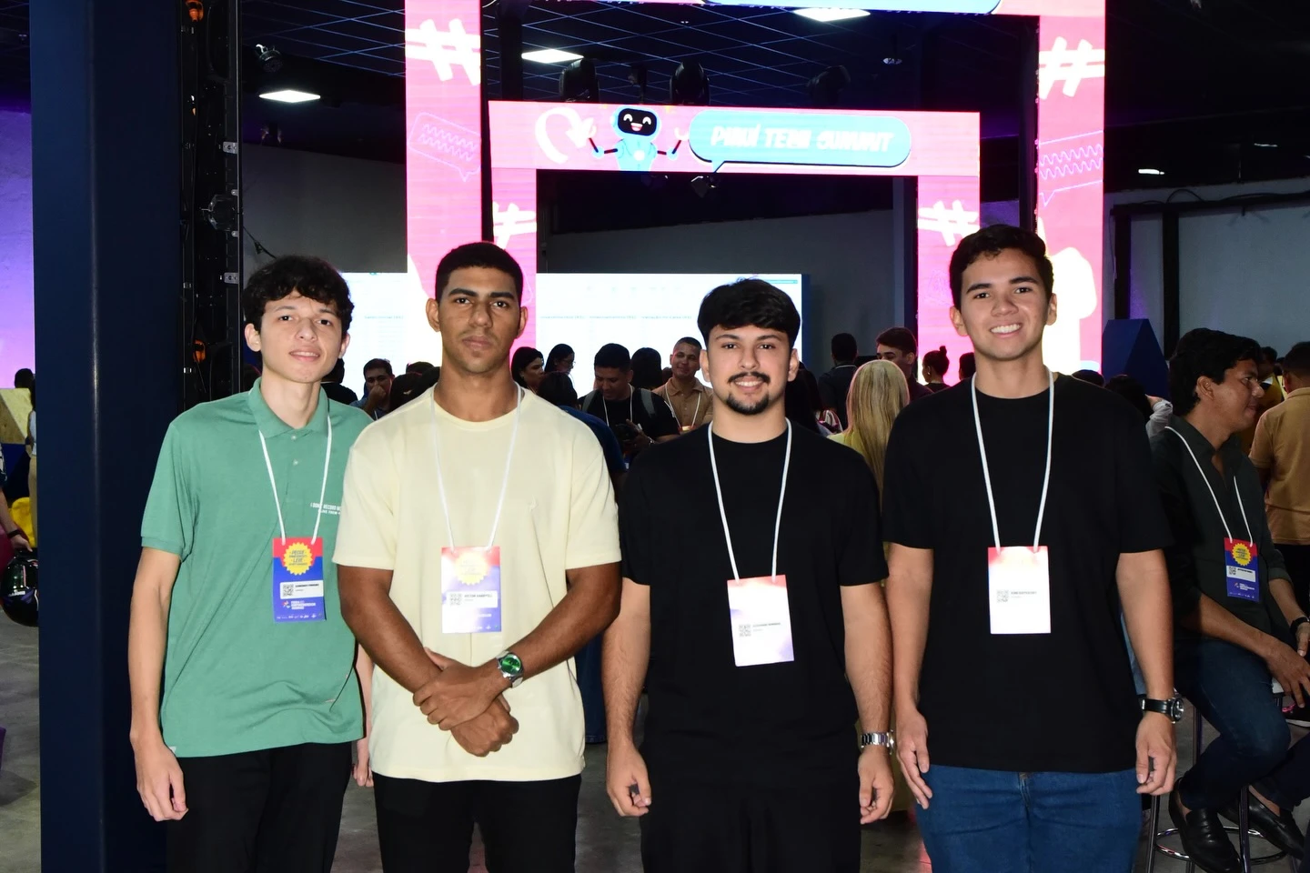 Quatro integrantes da equipe posam em frente a um portal luminoso da feira