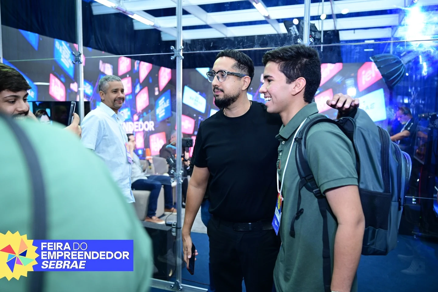 Integrante da equipe conversa com um participante em área envidraçada do evento